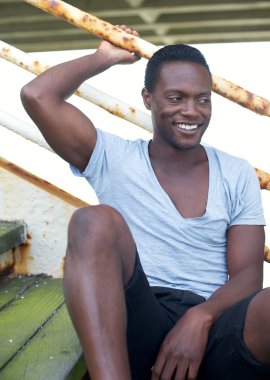 Afrika kökenli Amerikalı adam açık havada basamaklarında oturan gülümsüyor