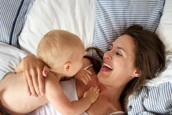 Portrait of a happy mother playing with baby in bed — Stock Photo, Image