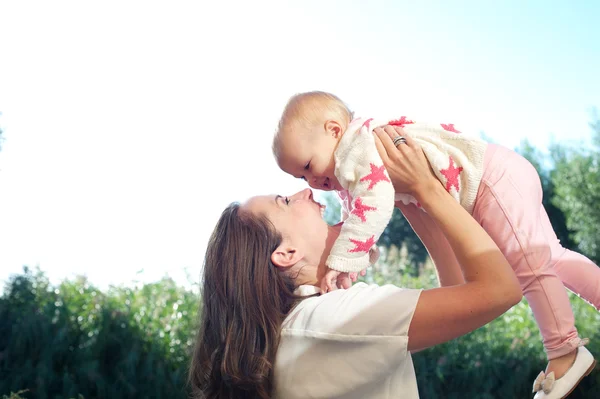 Portrait of a happy young mother lifting cute baby outdoors — Stock Photo, Image