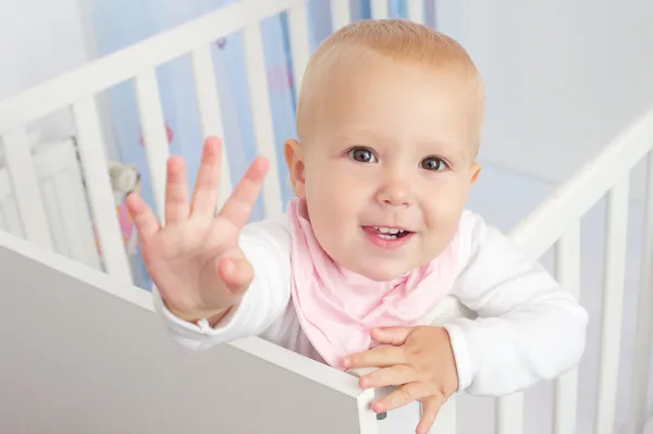 Retrato de um bebê bonito acenando Olá e sorrindo do berço — Fotografia de Stock