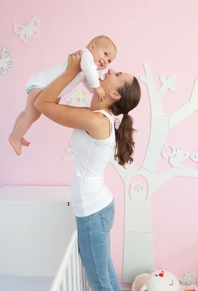 Happy young mother lifting cute baby out of crib — Stock Photo, Image