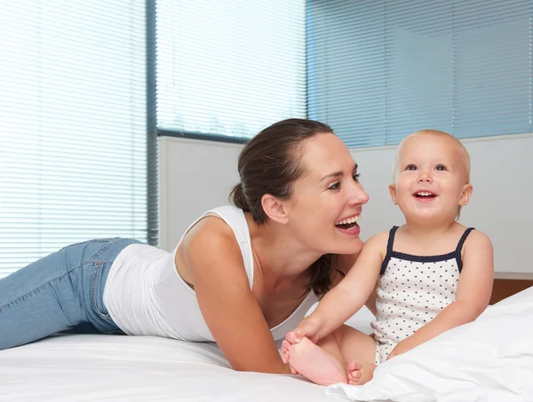 Hermosa madre riendo con lindo bebé en la cama — Foto de Stock