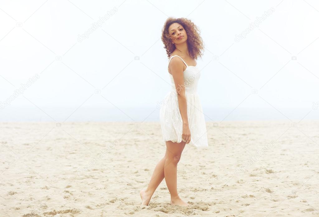 Beautiful woman in white dress walking on sand at the beach