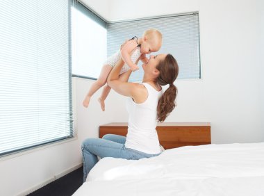 Happy mother playing with baby in bedroom