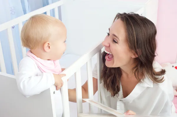 Portrait of a happy mother laughing with cute baby in crib — Stock Photo, Image
