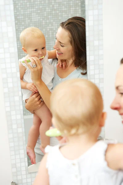 Hermosa madre enseñando a lindo bebé cómo cepillarse los dientes — Foto de Stock