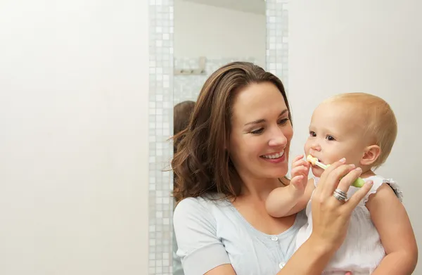Madre sonriente enseñando a bebé lindo a cepillarse los dientes con cepillo de dientes —  Fotos de Stock