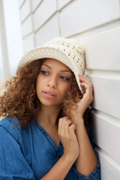 Beautiful young woman wearing hat and leaning against wall — Stock Photo, Image