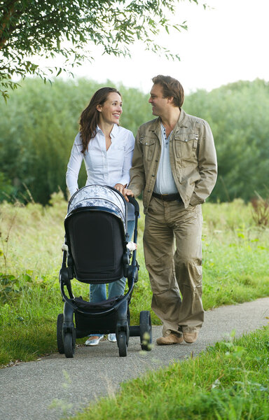 Happy mother and father pushing baby pram outdoors