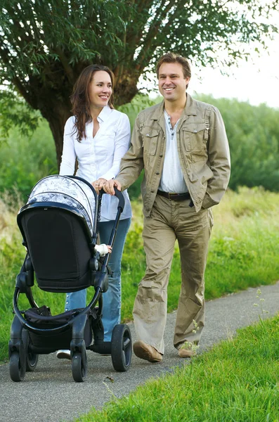 Mother and father walking outdoors with baby stroller — Stock Photo, Image