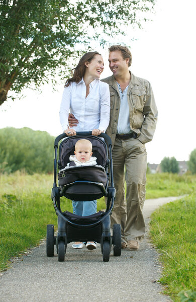Happy male and female parents walking with their child in baby carriage