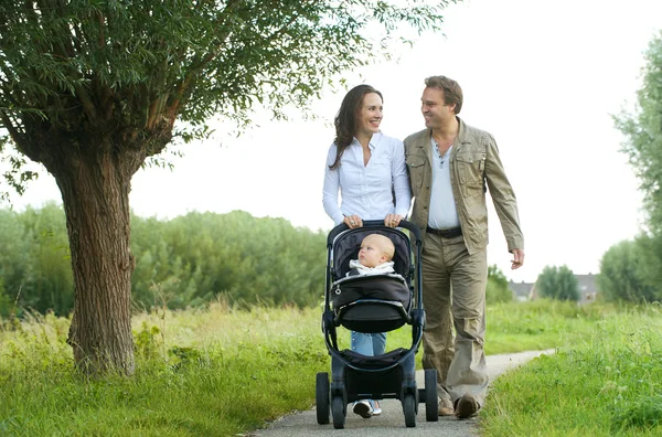 Happy mother and father walking with baby in pram — Stock Photo, Image