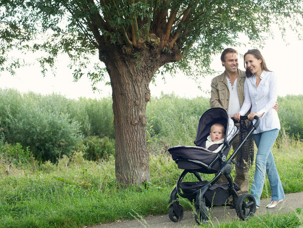 Mother and father walking outdoors and pushing baby in pram