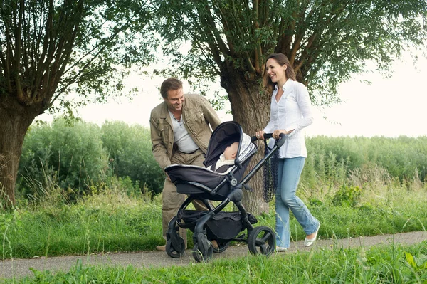 Счастливые мама и папа гуляют на улице с ребенком в коляске — стоковое фото