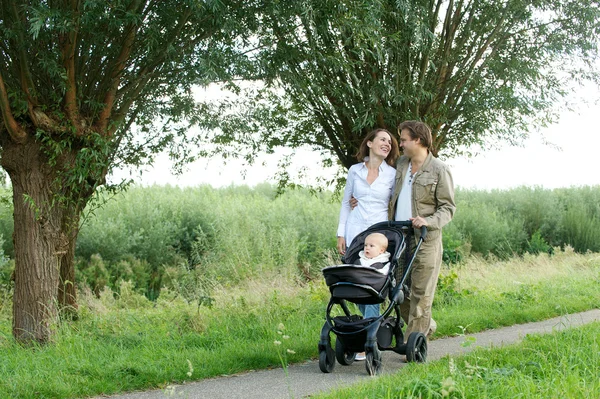 Young mother and father walking outdoors with baby in pram — Stock Photo, Image