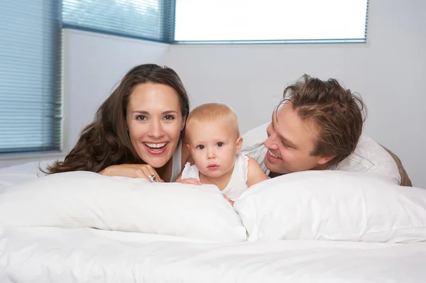 Retrato de una familia joven y feliz acostada en la cama con un bebé lindo —  Fotos de Stock