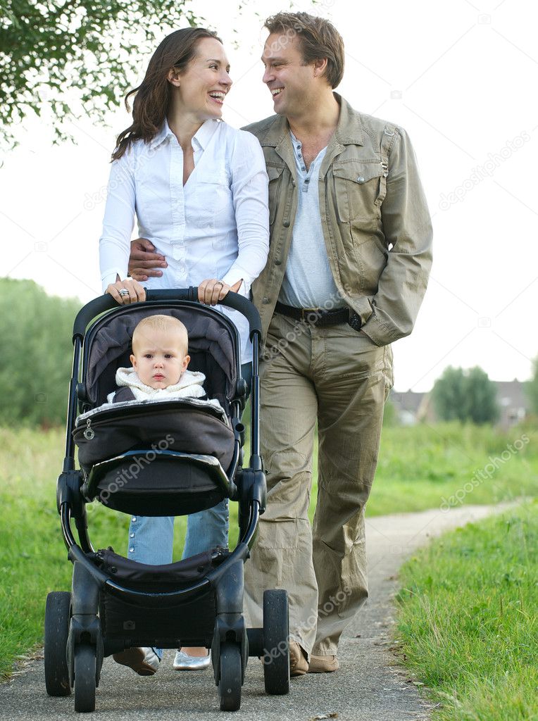 Happy mother and father smiling and pushing baby pram with child