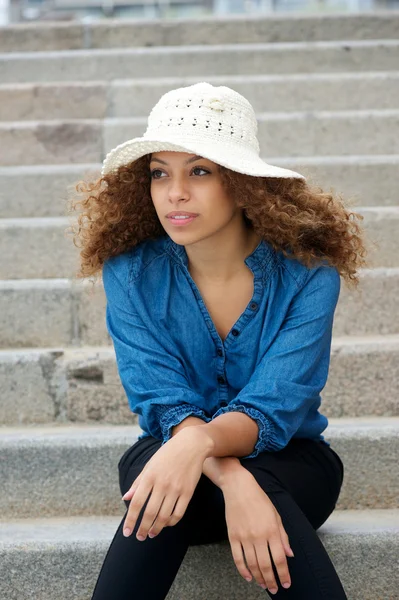 Young woman wearing white hat sitting alone outdoors — Stock Photo, Image
