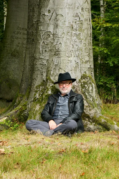 Gammal man sitter under träd i parken — Stockfoto