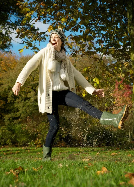 Carefree young woman kicking puddle of water in the park — Stock Photo, Image