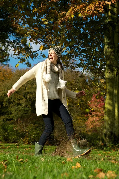 Carefree woman walking in the park and kicking a puddle of water — Stock Photo, Image