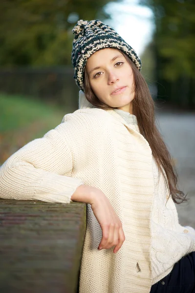 Mujer joven sentada sola al aire libre con suéter y sombrero —  Fotos de Stock