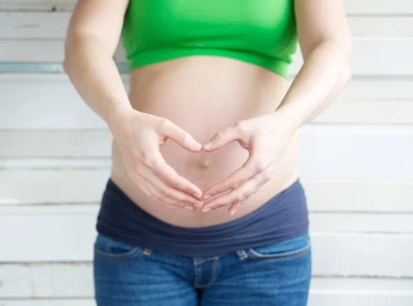 Pregnant woman showing heart shape with hands in front of stomach — Stock Photo, Image