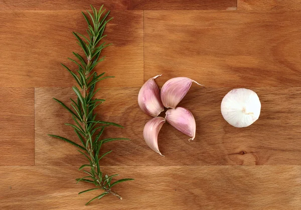 Cloves of garlic and fresh organic rosemary on wooden chopping board — Stock Photo, Image