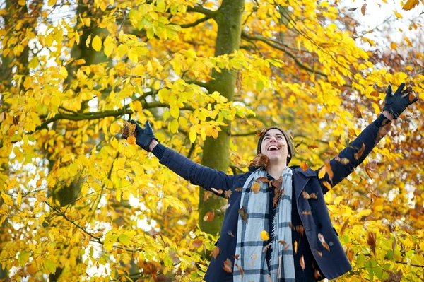 Boldog fiatalember mosolyogva, és dobott levelek, tárt karokkal — Stock Fotó