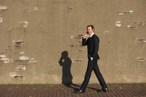 Lächelnder Geschäftsmann geht und telefoniert — Stockfoto