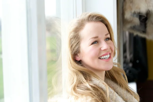 Jonge vrouw leunend tegen venster binnenshuis — Stockfoto