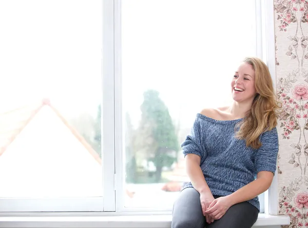 Mujer sonriente sentada junto a la ventana — Foto de Stock