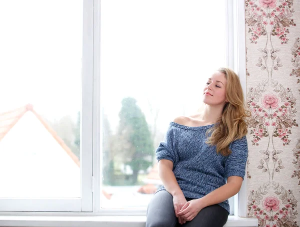 Piękna kobieta siedzi przez okno w domu — Zdjęcie stockowe