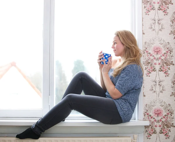 Sitting on windowsill with a cup of tea — Stock Photo, Image