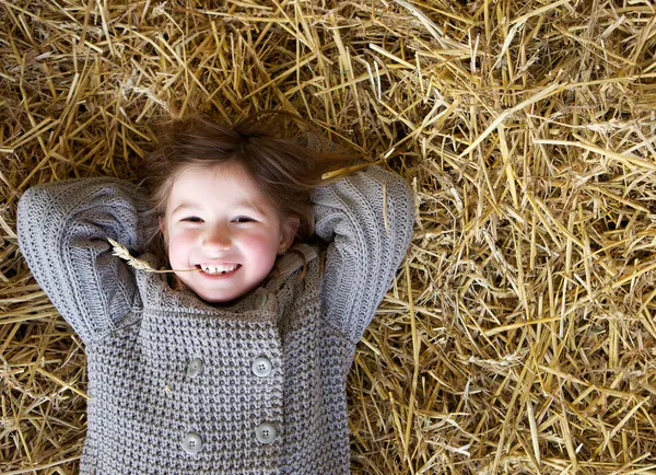 Girl smiling and lying down on hay — Stock Photo, Image