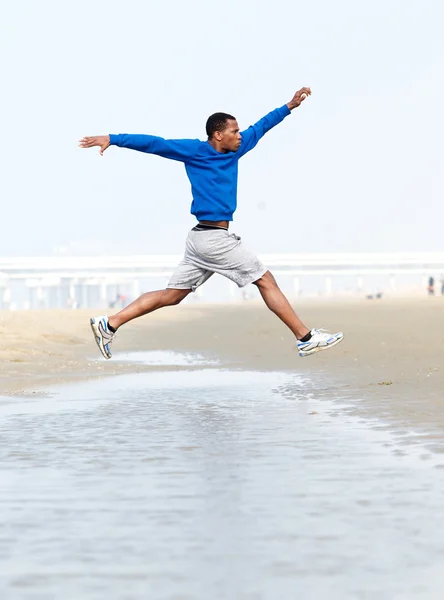 Atletische man uitgevoerd en springen op strand — Stockfoto