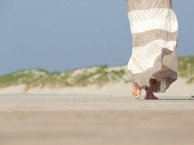 Barefoot woman walking away at the beach clipart