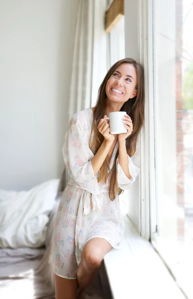 Kobieta uśmiechając się przez okno, picie herbaty — Zdjęcie stockowe