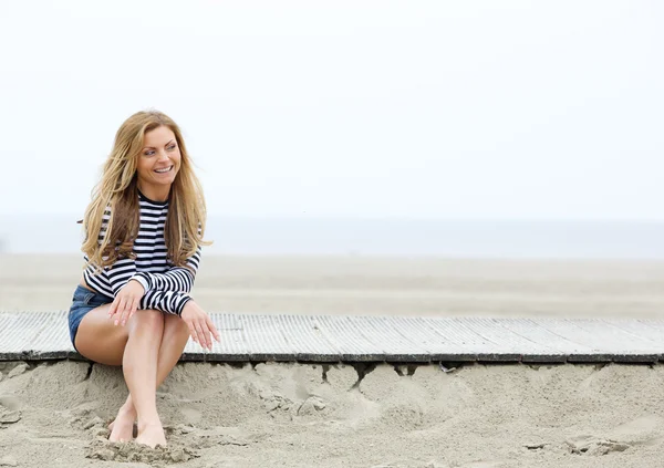 Uśmiechnięte młode blond kobieta siedzi na plaży — Zdjęcie stockowe