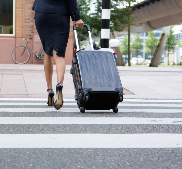 Businesswoman crossing street with luggage — Stock Photo, Image