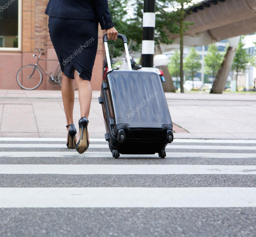 Businesswoman crossing street with luggage 