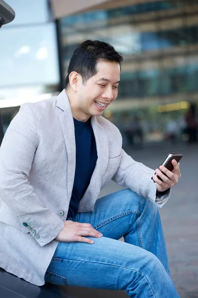 Azjatycki człowiek uśmiechający się z cellphone — Zdjęcie stockowe