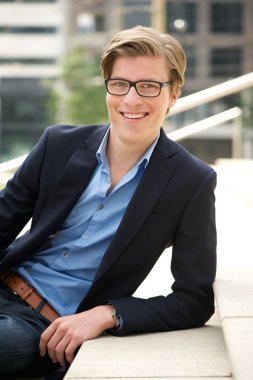 Gözlüklü genç adam gülümsüyor.