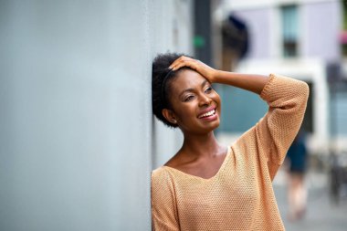 Portrait beautiful young black woman leaning against wall smiling with hand on head