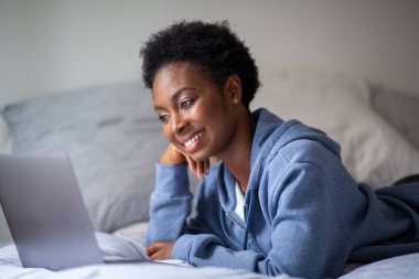 Portrait attractive young african American woman looking at laptop while lying in bed