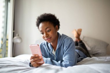Portrait young African American woman lying in bed looking at cellphone
