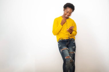 Portrait young African American woman holding mobile phone and listening with earphones