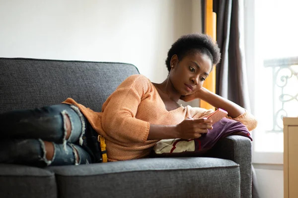Retrato Joven Mujer Negra Relajándose Sofá Casa Mirando Teléfono Celular —  Fotos de Stock