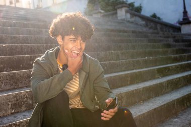 Portrait happy young guy sitting outside with mobile phone