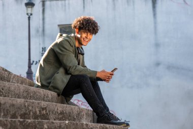 Full length profile portrait smiling teenage guy sitting on steps with cellphone